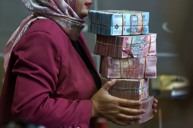 A teller, seen through a window, holds rupiah bank notes at a money changer in Jakarta on April 9, 2025. 