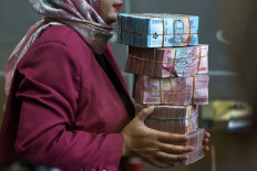 A teller, seen through a window, holds rupiah bank notes at a money changer in Jakarta on April 9, 2025. 