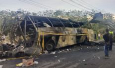 Local residents look at the burned-out frame of a bus operated by Antar Lintas Sumatera (ALS), draped with police tape, along the Trans-Sumatra Highway in Karang Jaya district of South Sumatra&rsquo;s North Musi Rawas regency on May 6, 2026, after a collision with a tanker truck that killed 16 people, including the drivers of the two vehicles.