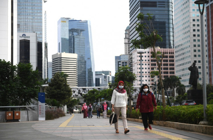 Office workers and other pedestrians stroll along a sidewalk on April 16, 2020, along Jl. Sudirman in downtown Jakarta.