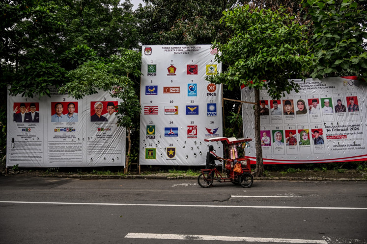 An ice cream vendor stops to look at posters of the three presidential and vice-presidential candidates, the list of participating parties and the list of candidates for members of the Regional Representative Council (DPD) from East Java on Feb. 3, 2024, in Surabaya, East Java, ahead of the 2024 presidential and legislative polls.