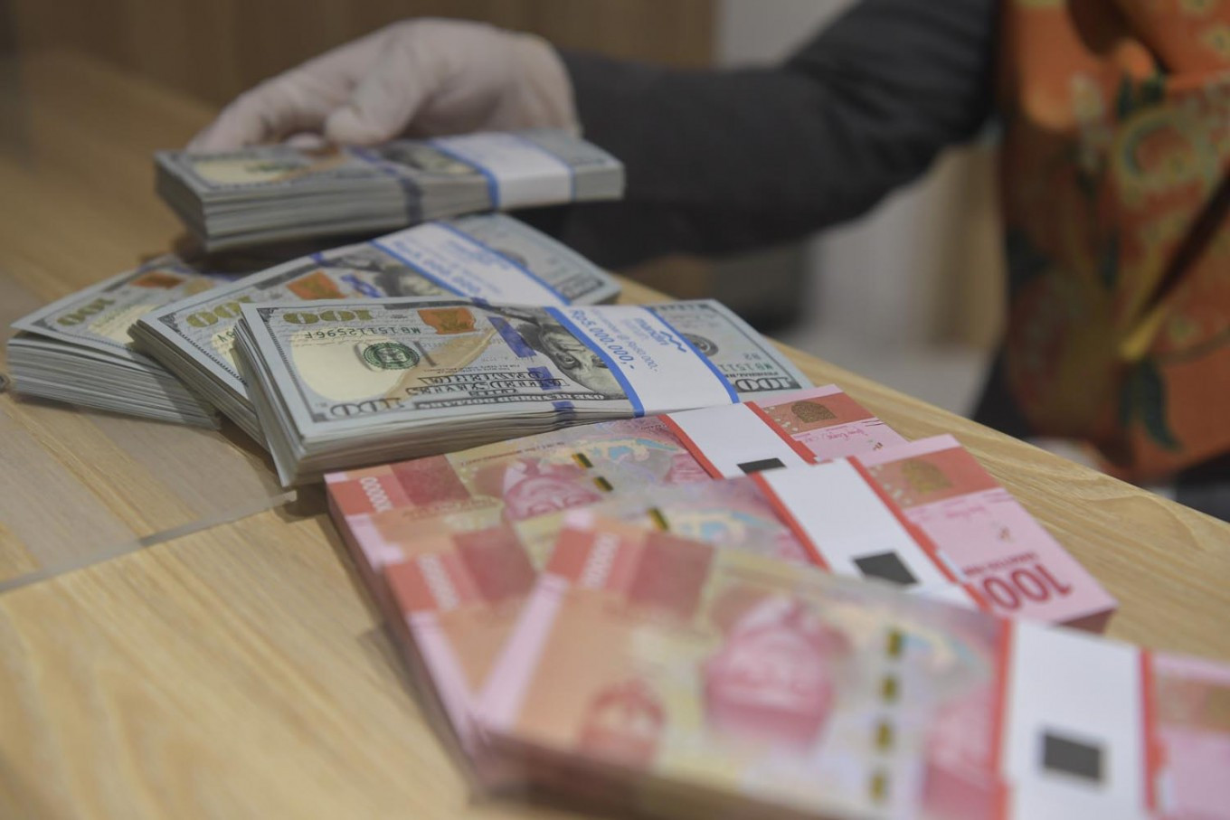 An employees shows rupiah and US dollar banknotes at a Bank Mandiri Syariah branch in Jakarta in this undated photo.
