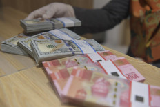 An employees shows rupiah and US dollar banknotes at a Bank Mandiri Syariah branch in Jakarta in this undated photo.