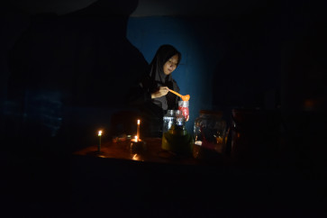 A vendor prepares drinks for customers in the dim light of candles on May 23, 2026, during a power outage in Nagari Kasang, Padang Pariaman regency, West Sumatra.