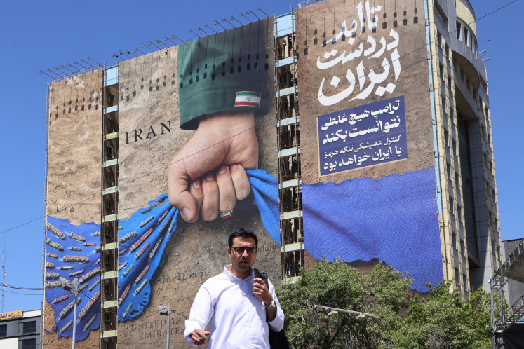 Echoes of Persian power: A man crosses a street past a billboard on the facade of a building depicting the Strait of Hormuz with a caption in Persian reading &ldquo;Forever in Iran&rsquo;s Hand&rdquo;, on Monday, May 25, 2026, at Vanak Square in Tehran.