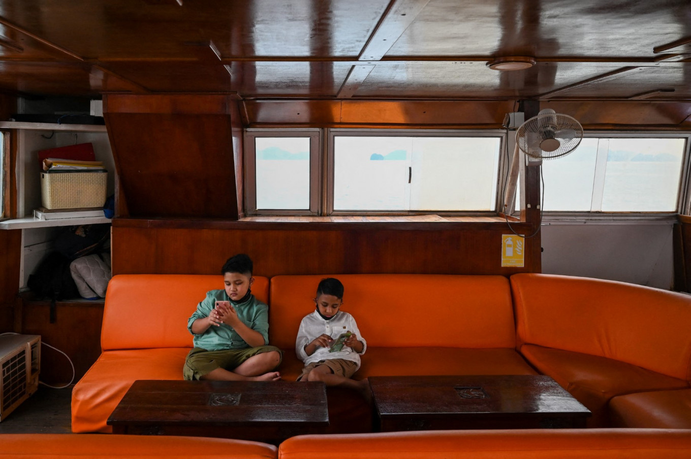 Two boys play with their mobile phones onboard a catamaran yacht in Langkawi, Malaysia, on September 17, 2021. 