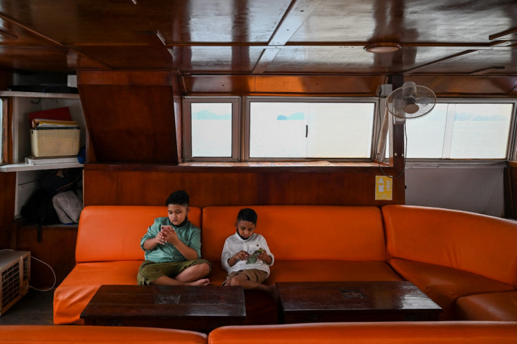Two boys play with their mobile phones onboard a catamaran yacht in Langkawi, Malaysia, on September 17, 2021. 