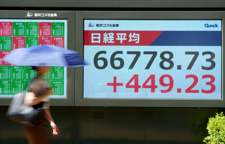 A woman walks past an electronic quotation board displaying the Nikkei Stock Average on the Tokyo Stock Exchange along a street in Tokyo on June 1, 2026.