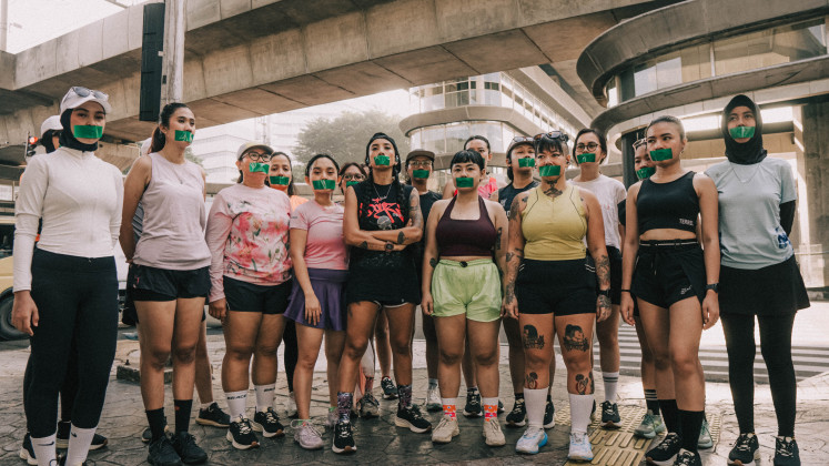 Muting, undone: Yacko (center, front row) stands among 18 other women, their mouths covered with green tape, in a still from the music video for &lsquo;Unbreakable Me&rsquo;, which premiered on YouTube on April 21, 2026, Kartini Day, and is dedicated &ldquo;To all the women who struggle to stay sane every day and heal through running&rdquo;.