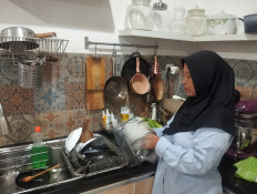 Holding on: Iti cleans kitchen utensils at the home of her employer, Vita Oktarina, in Depok, West Java, on the outskirts of Jakarta, on May 17, 2026. She began working as a domestic worker after her husband died in 2010.