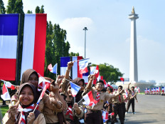 Schoolchildren pose with small Indonesian and French flags on May 28, 2025, while waiting to greet a motorcade carrying French President Emmanuel Macron at the National Monument (Monas) complex in Jakarta during his state visit to Indonesia.