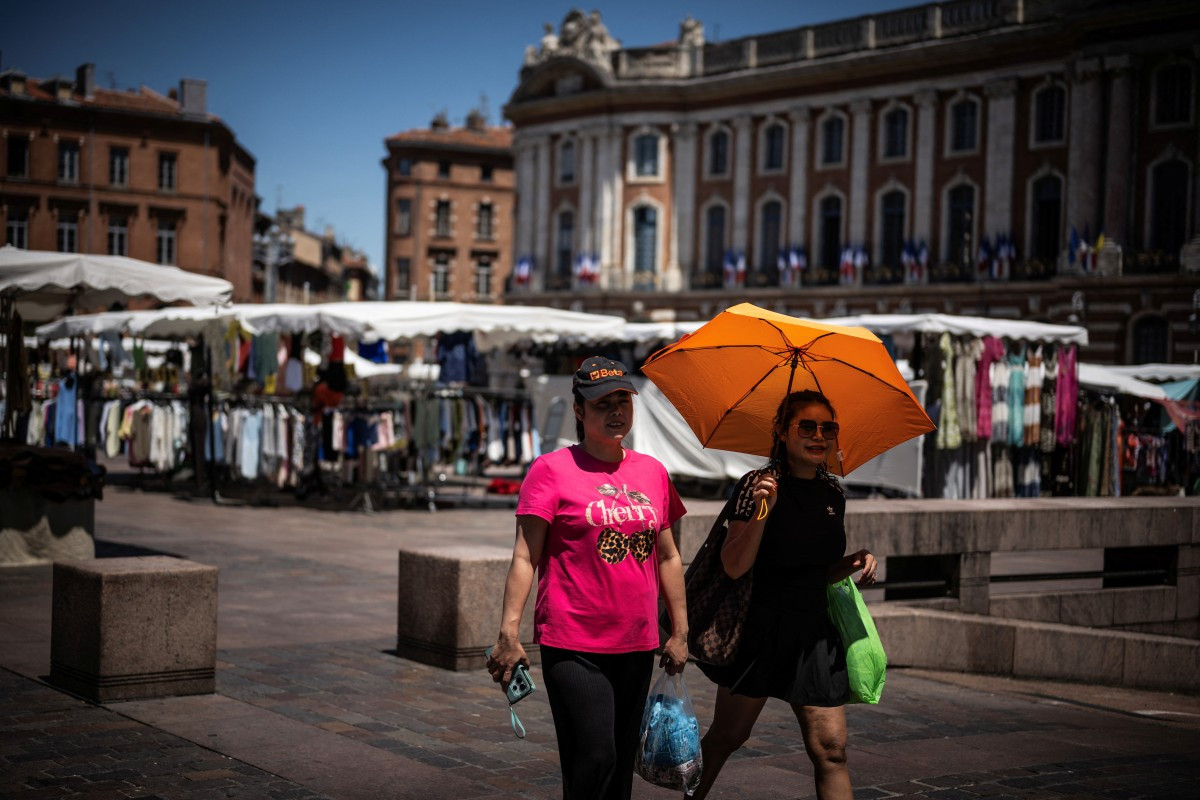 Pedestrians walk through the streets of Toulouse with an umbrella to protect themselves from the sun, on May 27, 2026, in Toulouse, southwestern France.