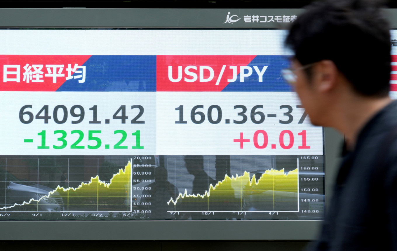 A man looks at electronic bulletin boards displaying the Nikkei 225 average on the Tokyo Stock Exchange (left) and the foreign exchange rate of the Japanese yen against the US dollar along a street in Tokyo on June 10, 2026.