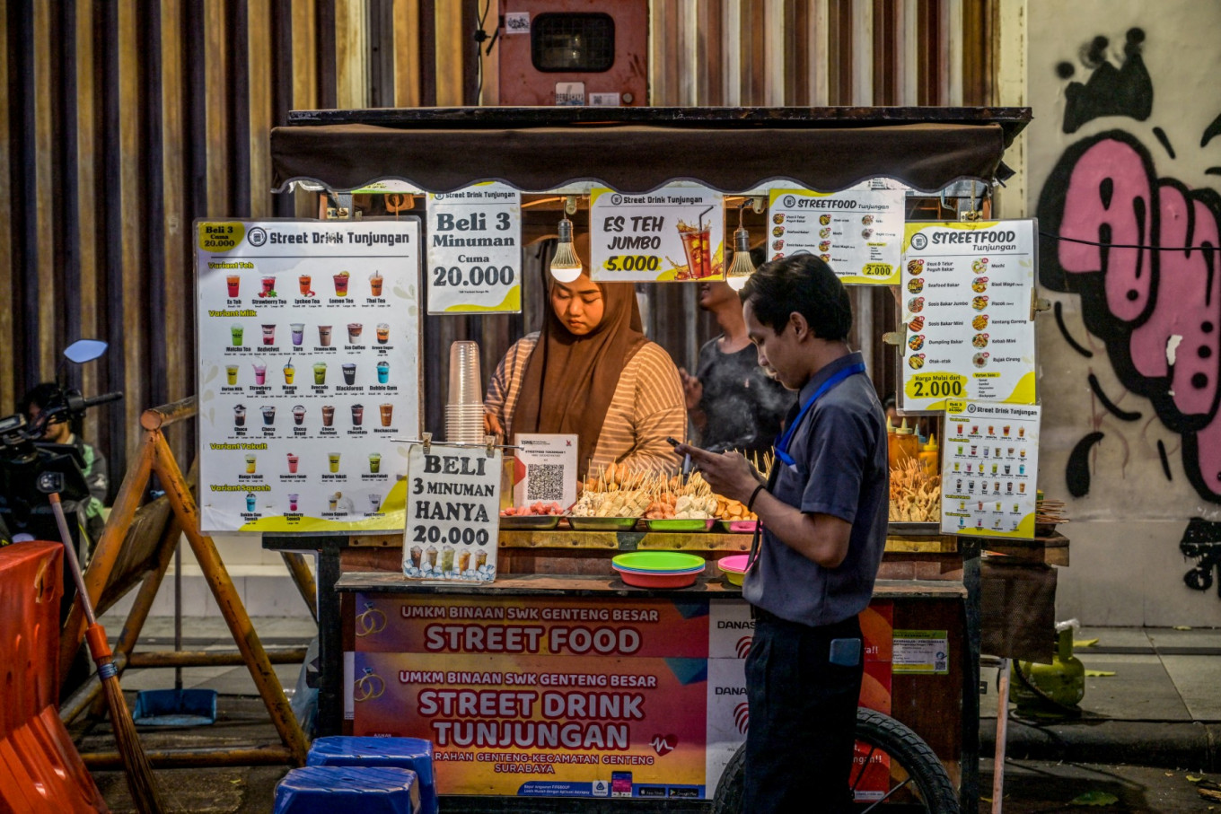 A woman selling sugary drinks serves customers on June 24, 2025, at a business district in Surabaya, East Java.
