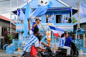 Argentina fan and fisherman Muhammad Yusuf (back, center) holds a replica of the World Cup trophy as football fans pass his house, painted in the colors of the Argentine national team, in a convoy welcoming the 2026 FIFA World Cup football tournament on the eve of its start in Polewali Mandar, West Sulawesi on June 11, 2026.