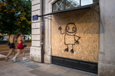 Passers-by walks past a building boarded up with graffiti-covered wooden panels on June 12, 2026 ahead of demonstrations against the nearby G7 summit in Evian, France. 