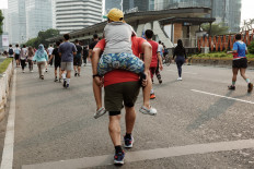 A man runs carrying a boy on his back on Aug. 24, 2025, on a street during Car Free Day in Jakarta.