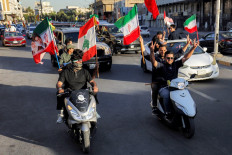 Youths ride scooters and vehicles while waving flags of Iraq, Iran, Lebanon and Hezbollah on June 15 in Baghdad, during celebrations following the announcement of a deal to end the war between Iran and the United States.