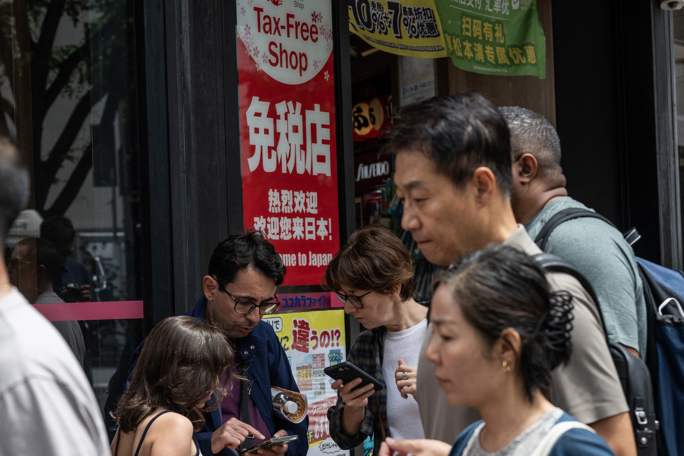 Tourists check their phones outside a tax free shop in Tokyo on June 23, 2026, as the weak yen continues to draw foreign shoppers. The yen, weighed down in particular by the prospect of monetary tightening by the US Federal Reserve (Fed), approached its lowest level in 40 years.