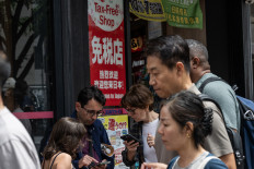 Tourists check their phones outside a tax free shop in Tokyo on June 23, 2026, as the weak yen continues to draw foreign shoppers. The yen, weighed down in particular by the prospect of monetary tightening by the US Federal Reserve (Fed), approached its lowest level in 40 years.