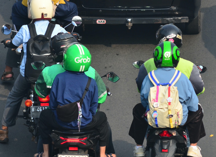 The logos of ride-hailing service providers Gojek and Grab are seen on helmets worn by two passengers using online motorcycle taxi services on June 24 in the Kampung Melayu Besar area of South Jakarta.
