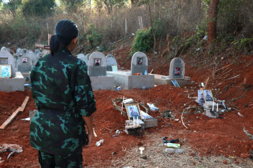 This file photo taken on March 6, 2025 shows an Urban Revolution Front (URF) soldier in front of gravestones of two URF soldiers killed by a Myanmar military drone attack in the forest near Moe Bye in Myanmar's eastern Shan State. More than 100,000 people have been killed across all sides in Myanmar since a military coup five years ago triggered civil war, a conflict monitor said July 1, 2026.