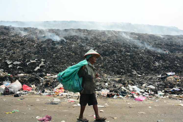 A scavenger walks in front of burning garbage at the Jatiwaringin landfill in Tangerang regency, Banten, on July 4, 2026.
