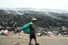 A scavenger walks in front of burning garbage at the Jatiwaringin landfill in Tangerang regency, Banten, on July 4, 2026.