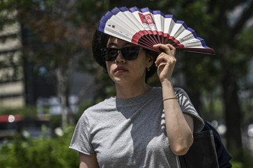 A woman uses a fan to shelter from the sun on a street in Seoul on July 12, 2026.