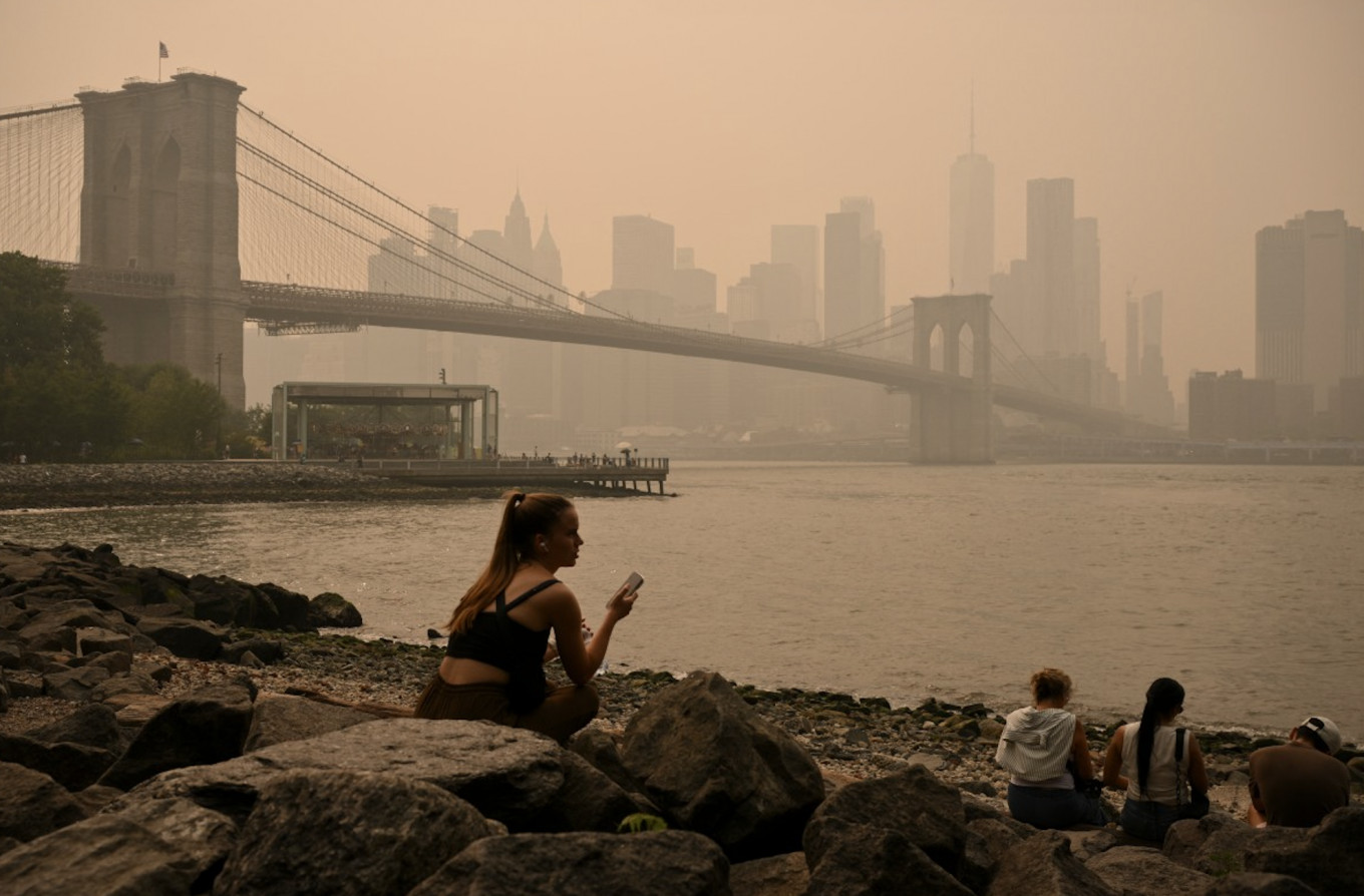 People sit near the Brooklyn Bridge as wildfire smoke from Canada causes hazy conditions on July 16, 2026 in New York.
