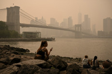 People sit near the Brooklyn Bridge as wildfire smoke from Canada causes hazy conditions on July 16, 2026 in New York.
