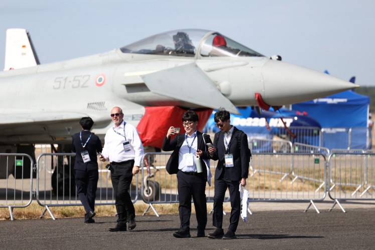 Delegates stand in front of an Italian Air Force Eurofighter Typhoon as they arrive to attend the opening day of the Farnborough International Airshow 2026 in in Farnborough, southwest of London, on Monday, July 20, 2026. 