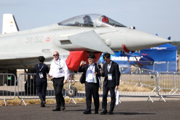 Delegates stand in front of an Italian Air Force Eurofighter Typhoon as they arrive to attend the opening day of the Farnborough International Airshow 2026 in in Farnborough, southwest of London, on Monday, July 20, 2026. 