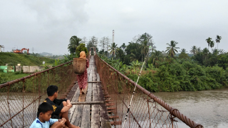 A Muara Maung resident in Lahat regency, South Sumatra, walks across a bridge to her farm on Oct. 19, 2025, as emissions from a nearby coal-fired power plant cloud the sky.