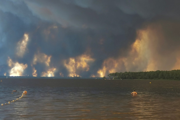 A beach goer stands in lake Lacanau, also called Etang de Lacanau (Lacanau Pond) from the beach of Moutchic in Lacanau, southwestern France on July 24, 2026, as clouds of smoke rise into the sky from a wildfire. The fire raging in the northern part of the Arcachon Basin in Gironde, southwest France, has swept through more than 3,400 hectares, according to the latest figures released by the prefecture.