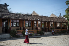Pupils carry free nutritious meal packages past a classroom with a collapsed roof at SD Tanggirejo state elementary school in Tegowanu, Grobogan, Central Java, on July 21, 2026. 