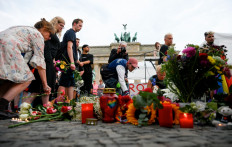 Mourners place bouquets of flowers on July 26, 2026 in front of landmark Brandenburg Gate during to a so-called &ldquo;community mourning&ldquo; one day after the car ramming attack on people on the outskirts of Berlin's Christopher Street Day (CSD) parade on late July 25, 2026, killing one person and injuring 16 in the Tiergarten park. 