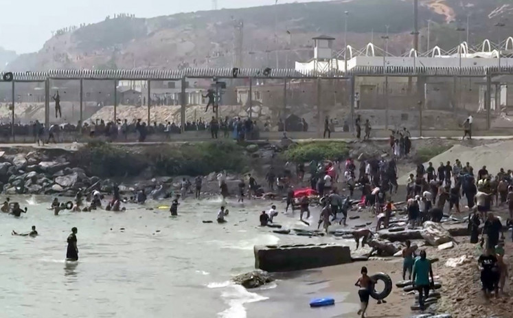 This video frame grab obtained from an AFP video shows migrants reaching the shore of Spanish north African exclave of Ceuta, after swimming around the border fence between Morocco and Spain, in Ceuta on July 30, 2026. Hundreds of migrants entered the Spanish north African exclave of Ceuta today, AFP reporters saw, many of them having swum by sea around the frontier fence. 