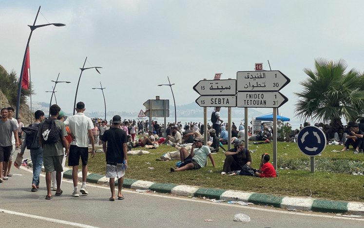 Migrants rest at a roundabout while waiting for a chance to cross to the Spanish enclave of Ceuta on the Moroccan side of the border in Fnideq, Morocco, on July 31, 2026.