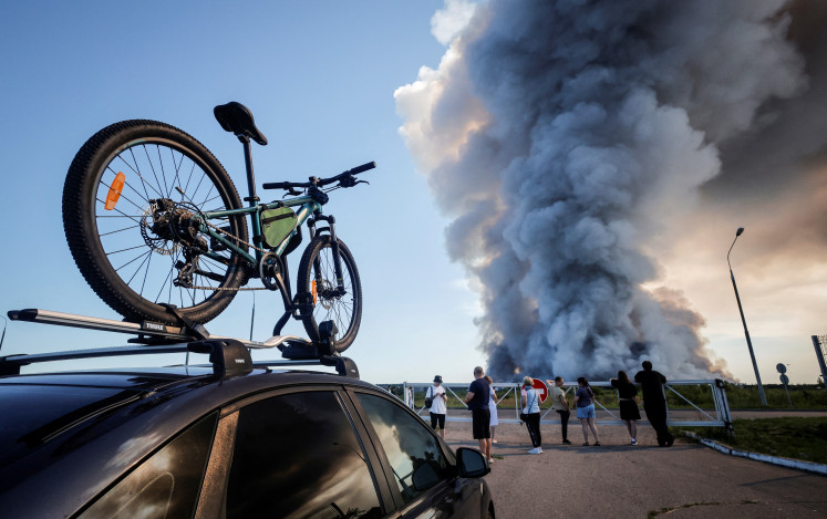 Bystanders watch as smoke rises from a fire at the Russian e-commerce firm Wildberries' logistics complexes in the town of Elektrostal outside Moscow on July 18, 2026. A Ukrainian drone attack on two logistics centres in Russia killed eight people and injured 24, officials said on July 18, 2026.