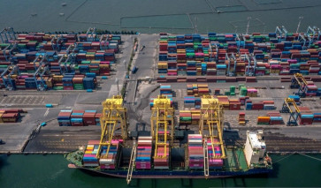 Export oriented: Using a rubber-tired gantry crane, port workers load export-bound containers onto a vessel flying a Portuguese flag on June 24, 2025, at Tanjung Mas port in Semarang, Central Java. 