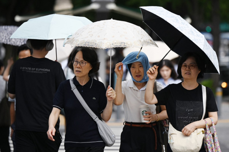 People shelter from the heat under umbrellas in Seoul on August 4, 2026. South Korea's summer heat has killed 16 people so far this year, the interior ministry said August 4, as the nation swelters in a wave of searing weather.