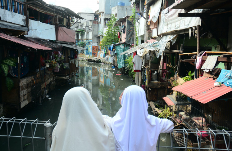 Two schoolgirls look at an informal riverbank settlement on Aug. 7, 2026, from a bridge in Kebon Melati village, Tanah Abang, Central Jakarta.