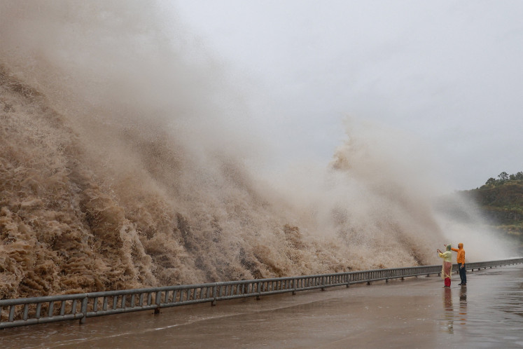 People stand next to huge waves crashing on a waterfront as Typhoon Dolphin approaches, in Sanmen county, Taizhou, Zhejiang province, China, August 8, 2026.