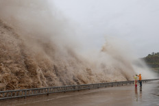 People stand next to huge waves crashing on a waterfront as Typhoon Dolphin approaches, in Sanmen county, Taizhou, Zhejiang province, China, August 8, 2026.
