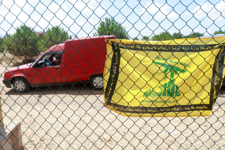 A flag with the pattern of the Hezbollah flag hangs on a fence as residents wait to enter the town of Zawtar al-Gharbiyeh in southern Lebanon on July 25, following the withdrawal of Israel forces under a United States-brokered plan.
