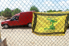 A flag with the pattern of the Hezbollah flag hangs on a fence as residents wait to enter the town of Zawtar al-Gharbiyeh in southern Lebanon on July 25, following the withdrawal of Israel forces under a United States-brokered plan.