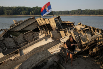 A woman stands on a sunken German warship from World War II, exposed due to low Danube river levels caused by drought and extreme heat near Prahovo, Serbia, on Aug. 13. 2026.