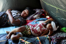 Caroline Cellomita Kasang, 3, who suffered a head injury after she was hit by a collapsed wall while escaping from a house during an earthquake, rests along with her grandmother Katarina Dadona, 58, at a makeshift medic-tent serving as temporary shelter for people affected by the earthquake in Reok, East Nusa Tenggara, on Aug. 18, 2026. 