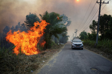 A car passes by next to flames as a wildfire burns in Rambutan village, Ogan Ilir regency, South Sumatra, on Aug.15, 2026. 